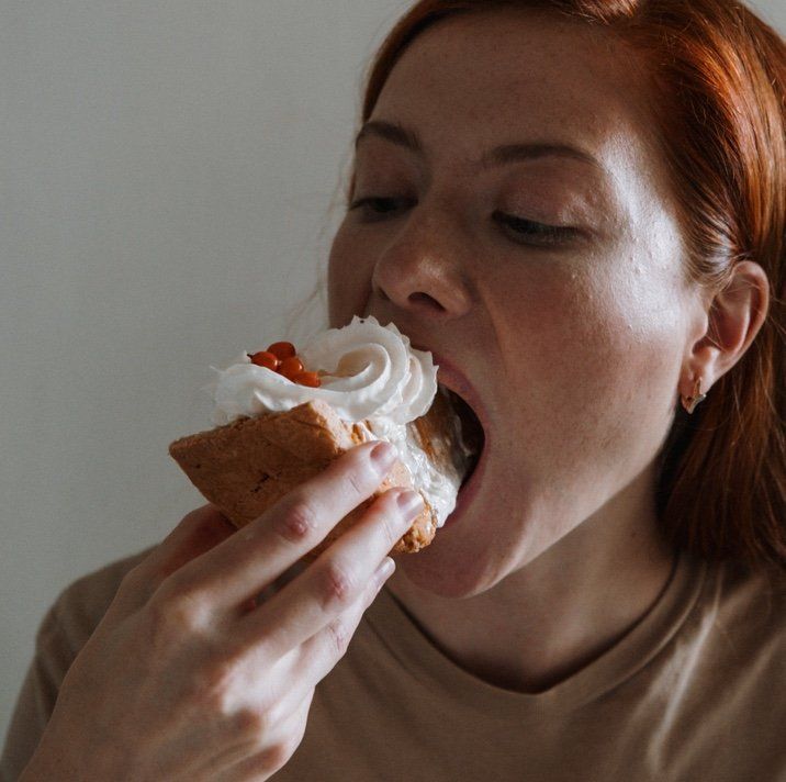 A woman is eating a piece of cake with whipped cream on top