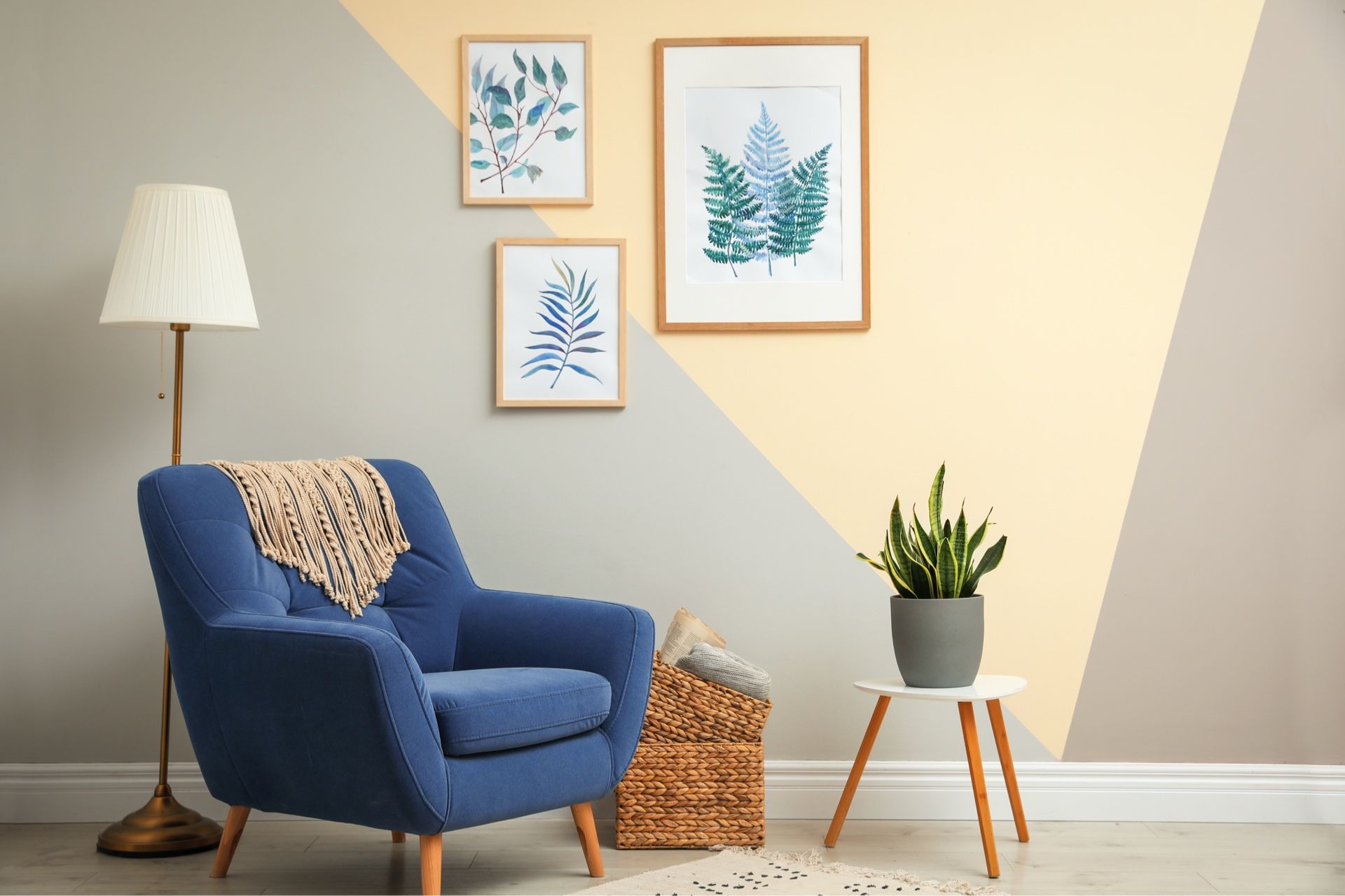 A living room with a blue chair , lamp , and paintings on the wall.