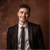 Smiling man in a dark suit and tie against a warm brown studio backdrop