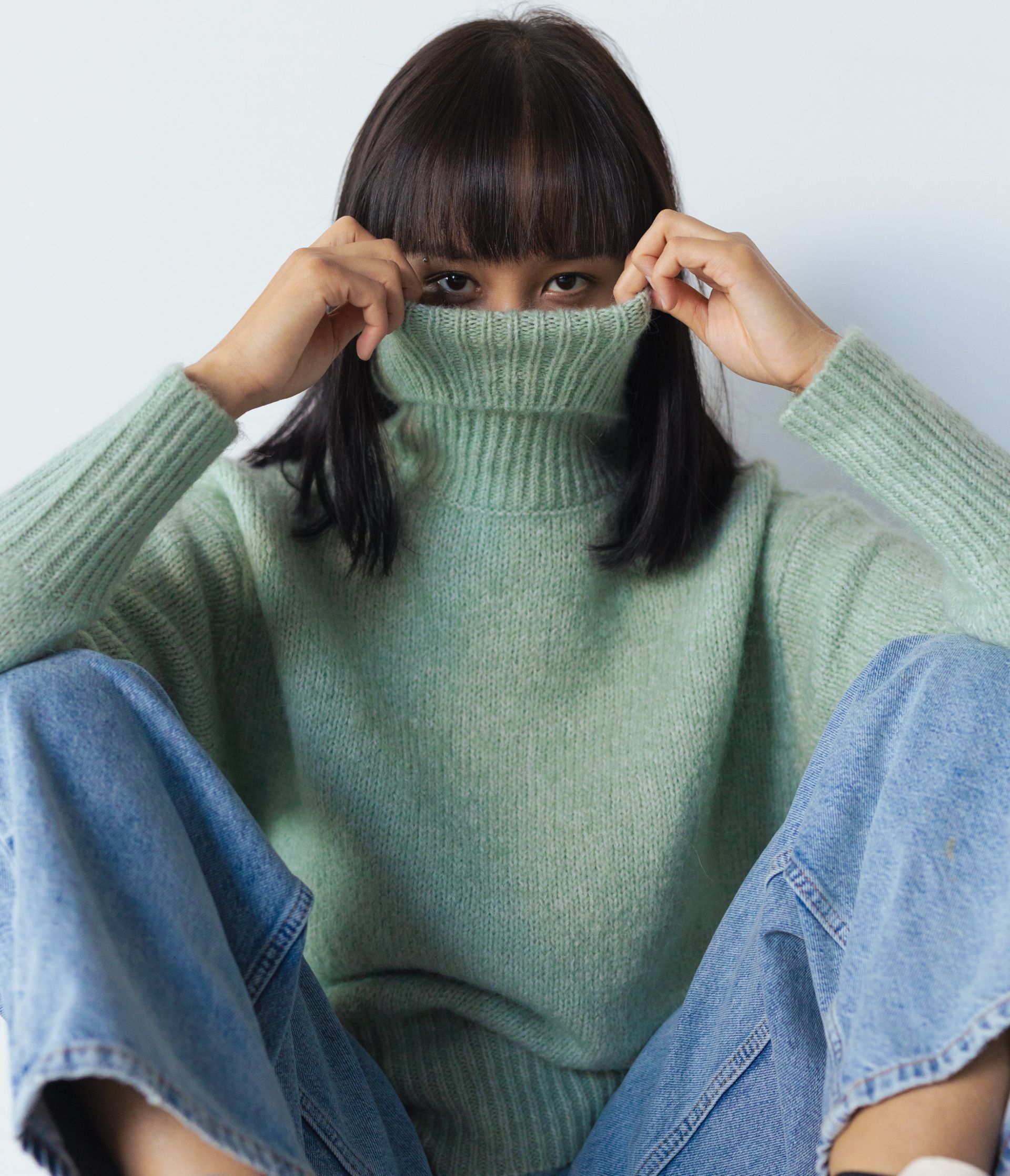 A woman wearing a green sweater covering her face with her hands
