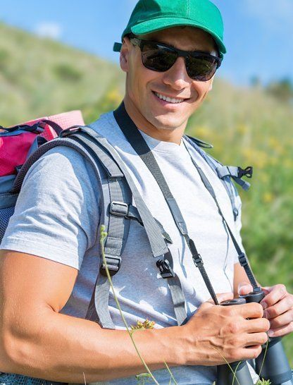 A man with a backpack and binoculars is standing in a field.