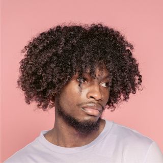 A man with curly hair and a beard is wearing a white shirt.