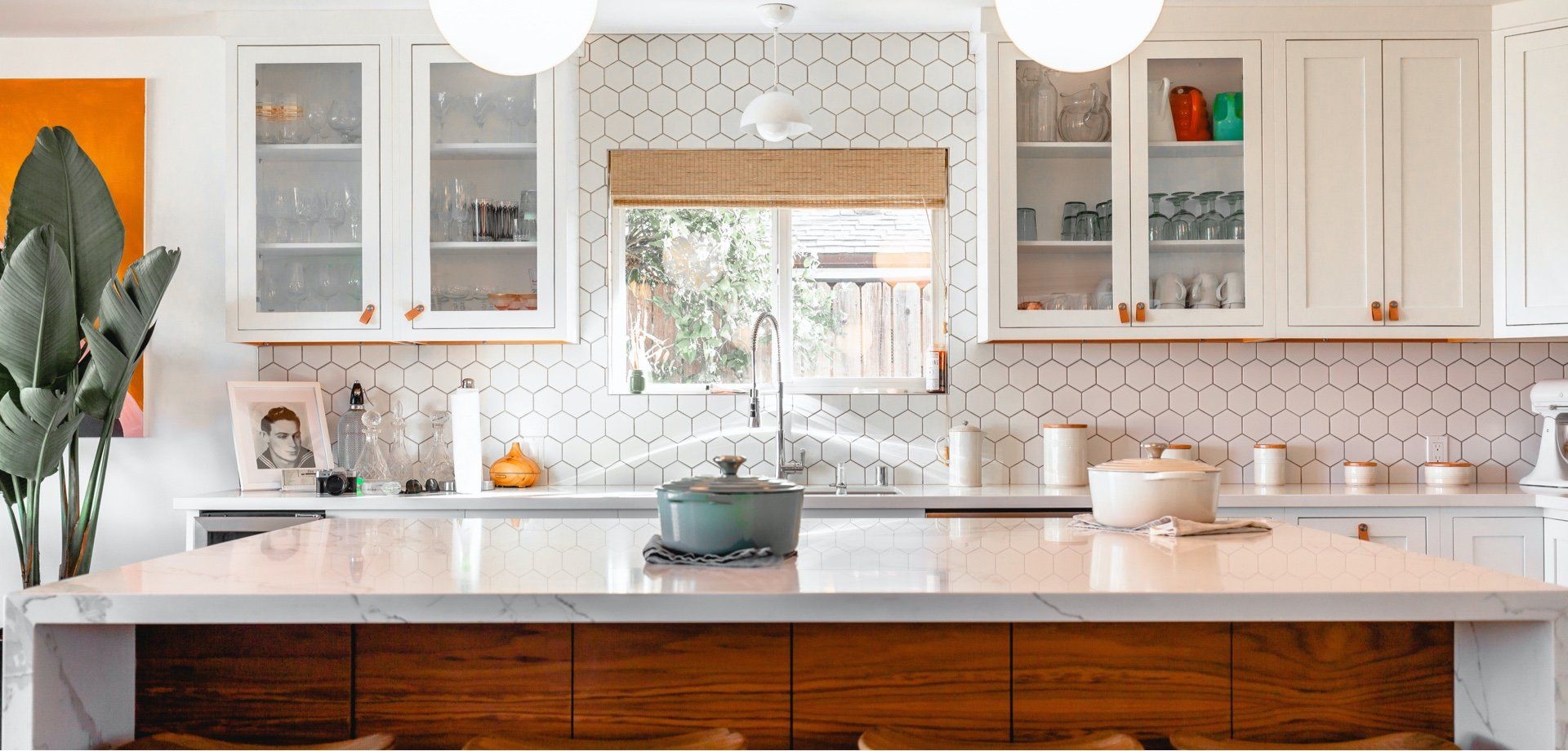 A kitchen with white cabinets , a large island , a pot on the stove and a window.