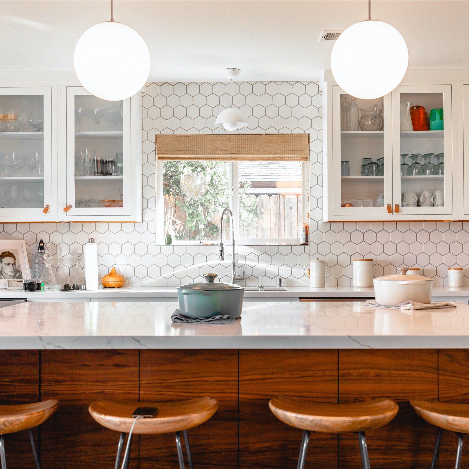 Bright modern kitchen with white cabinets, wood island, pendant lights, and three wooden stools