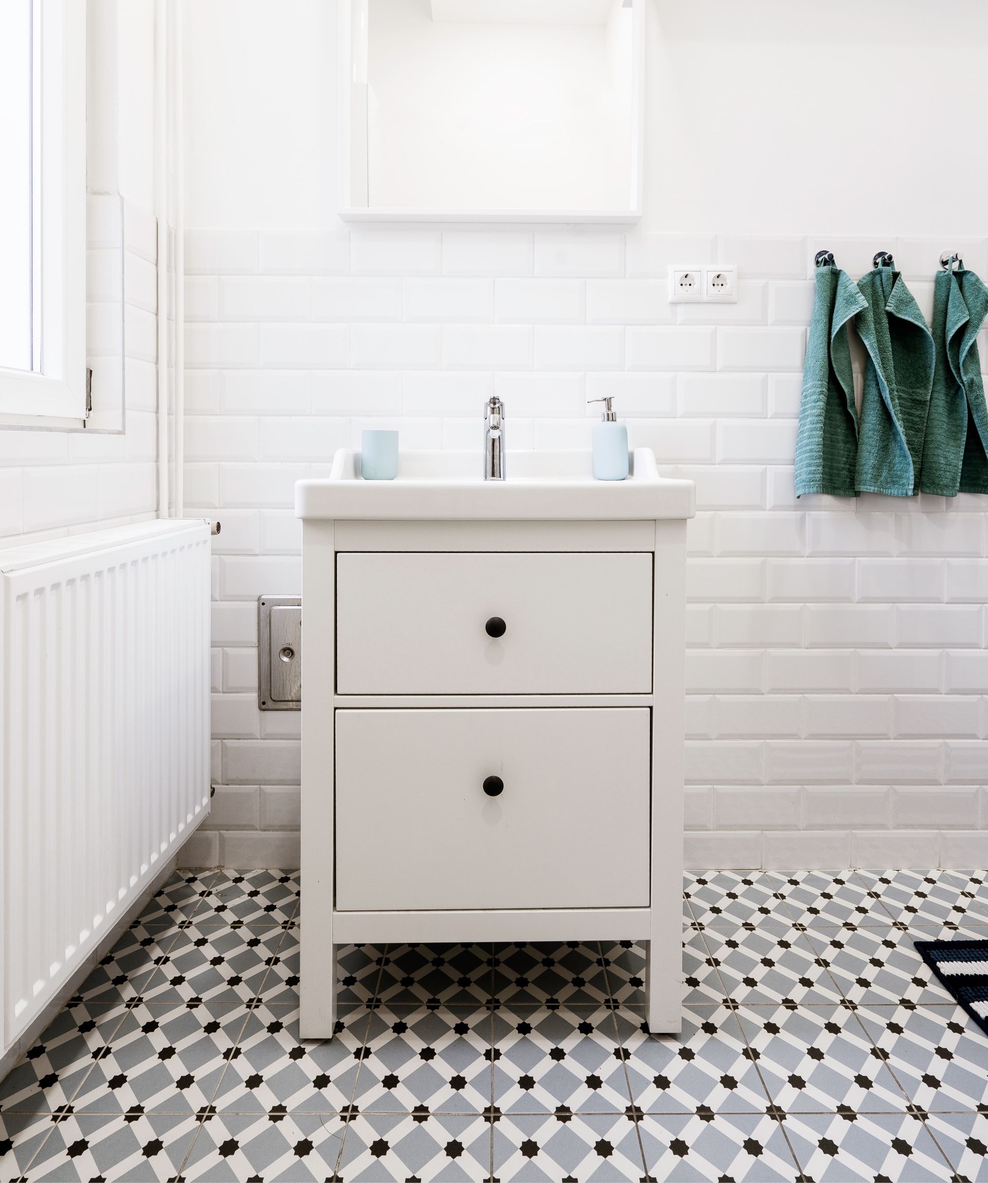 White bathroom with vanity, tiled walls and floor, and green towels.