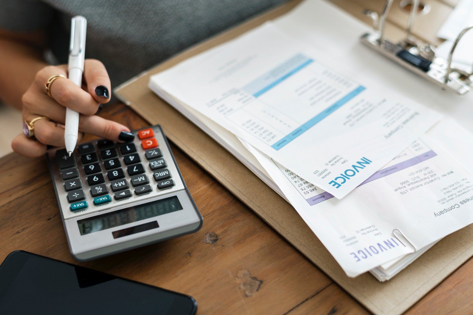 A woman is using a calculator and writing on an invoice.