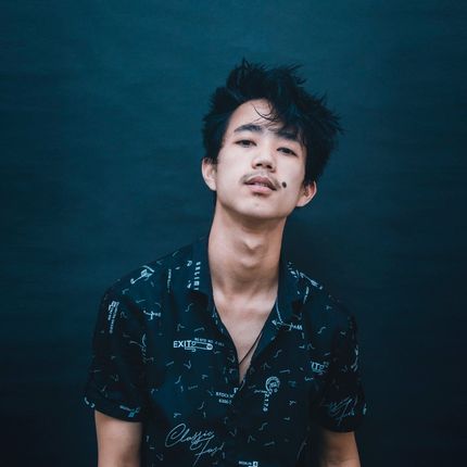 A young man in a black shirt is standing in front of a black wall.