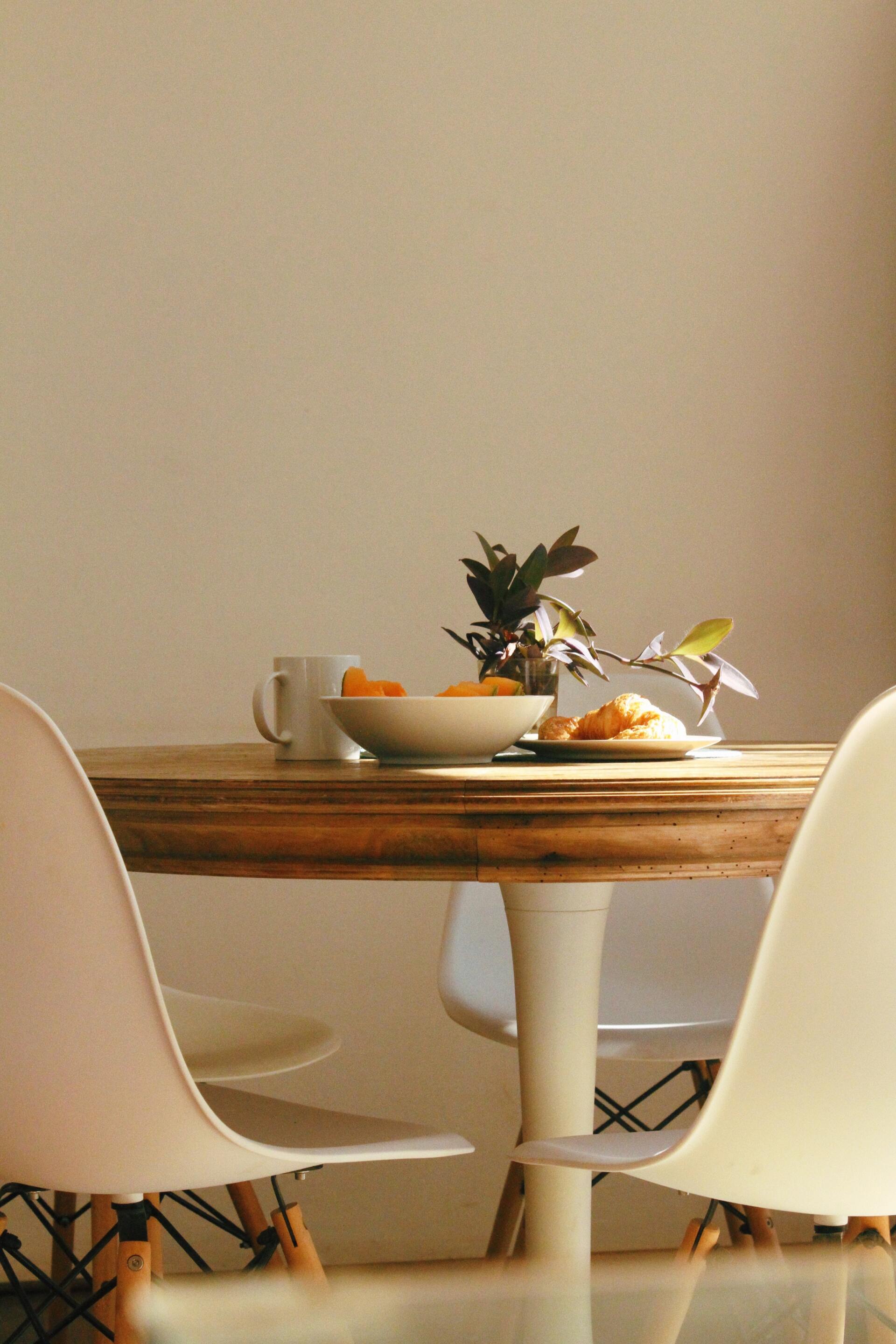 A wooden table with two white chairs and a bowl of fruit on it.