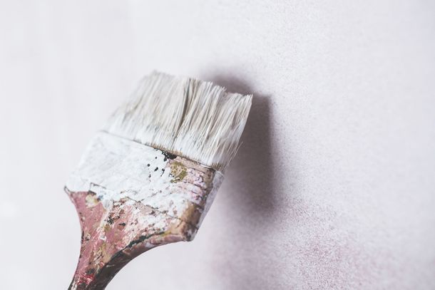 A paint brush with white paint on it is sitting on a white wall.