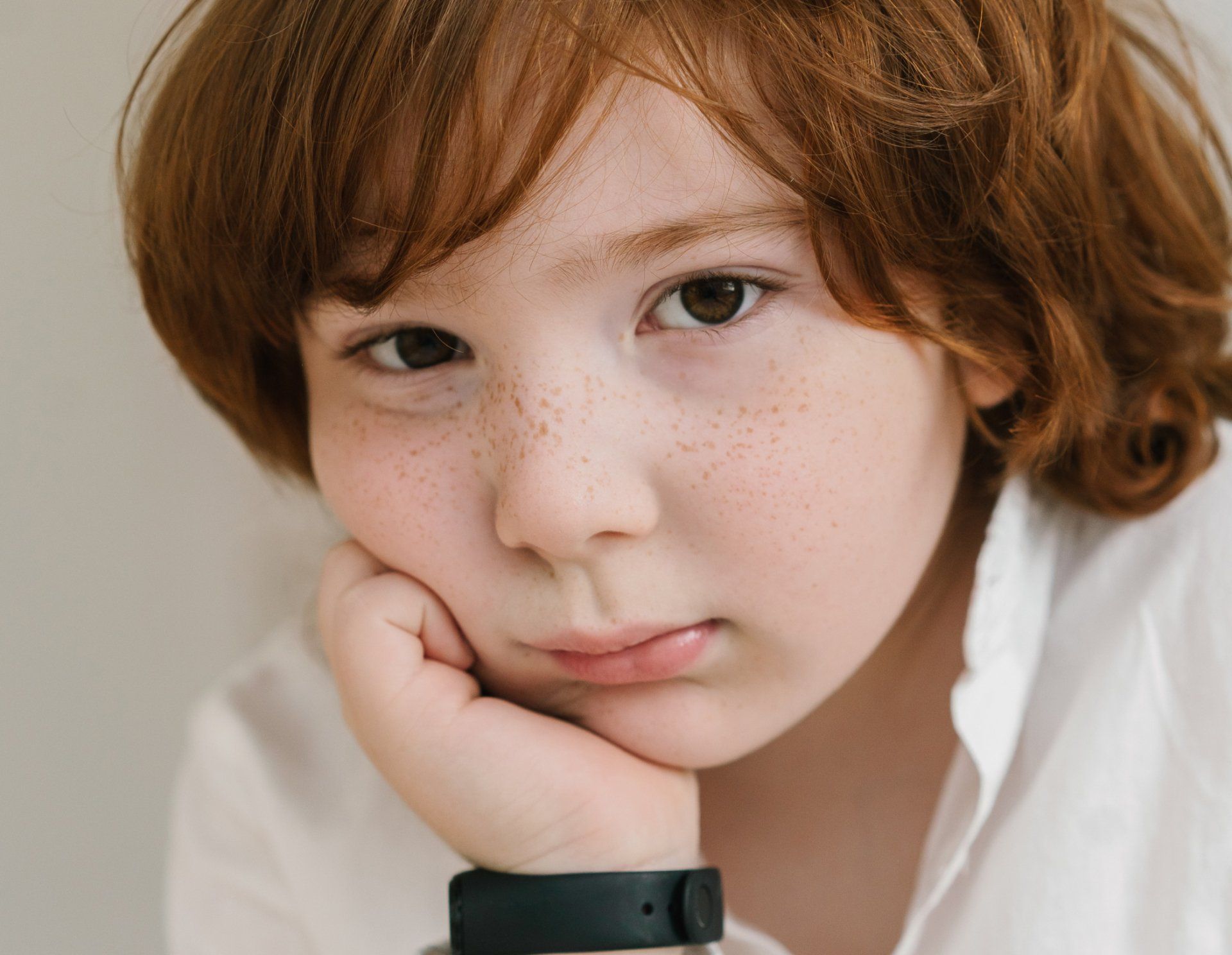 A young boy with red hair and freckles is wearing a watch on his wrist.