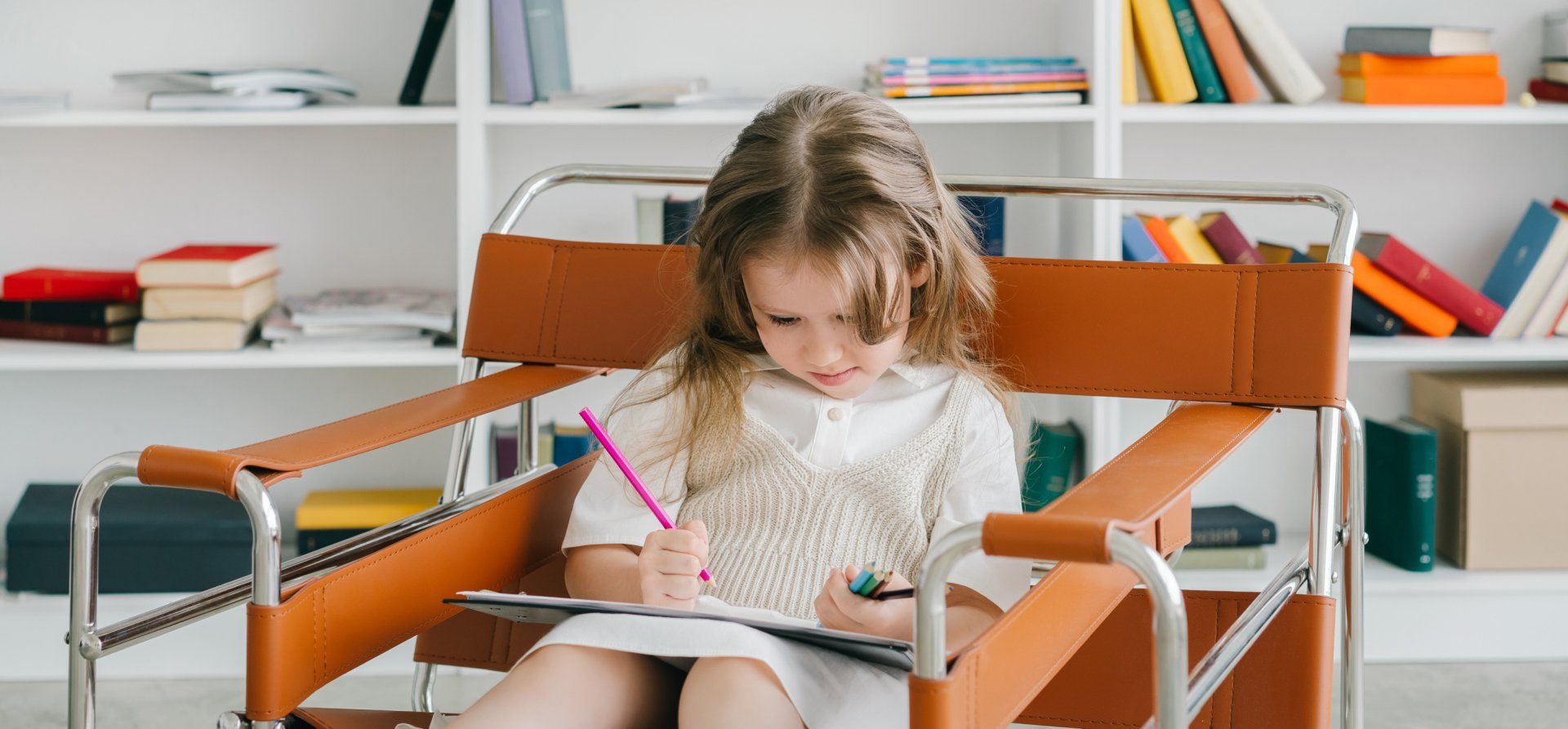 A little girl is sitting in a chair writing in a notebook.