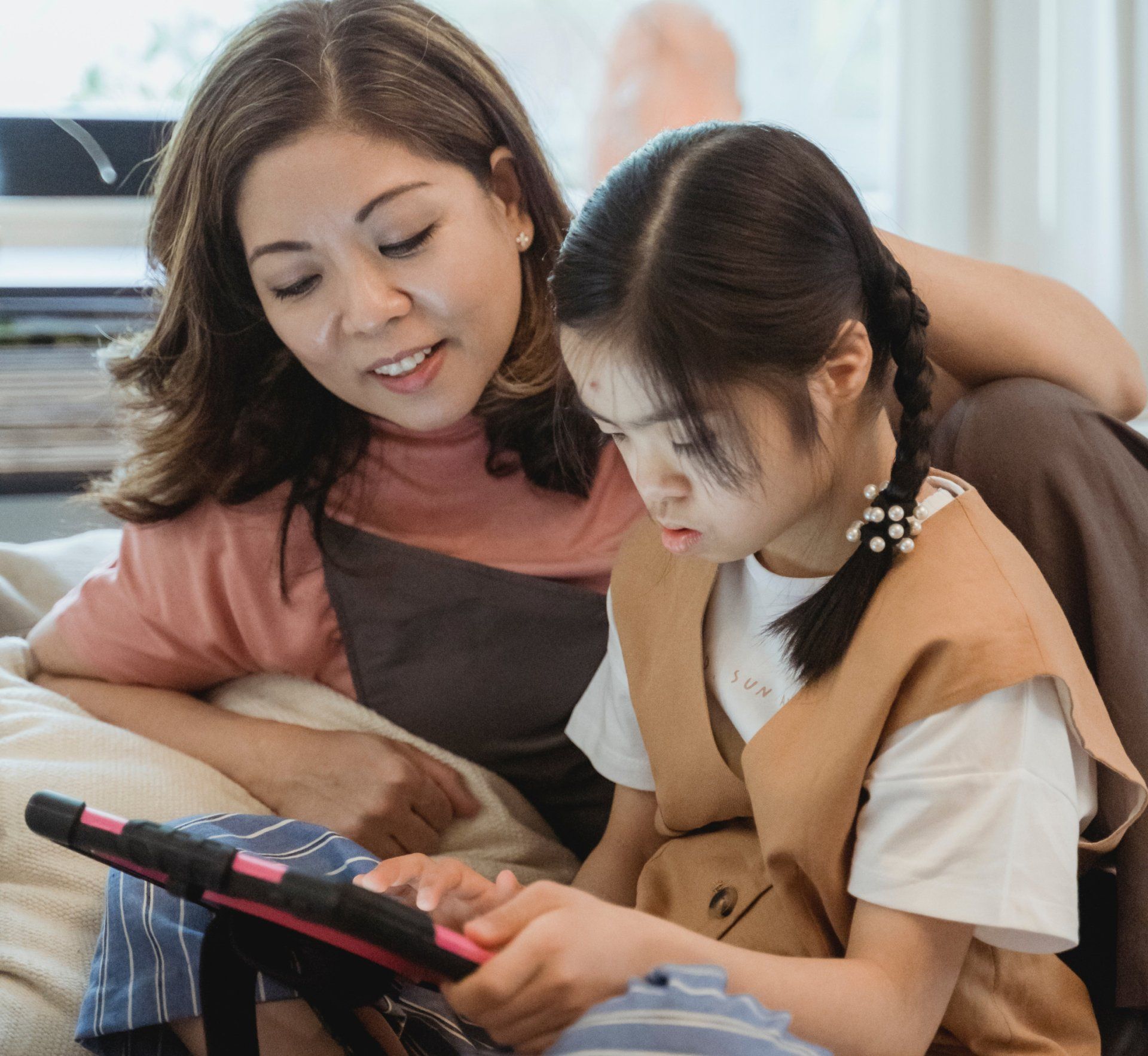 A woman and a little girl are sitting on a couch looking at a tablet.