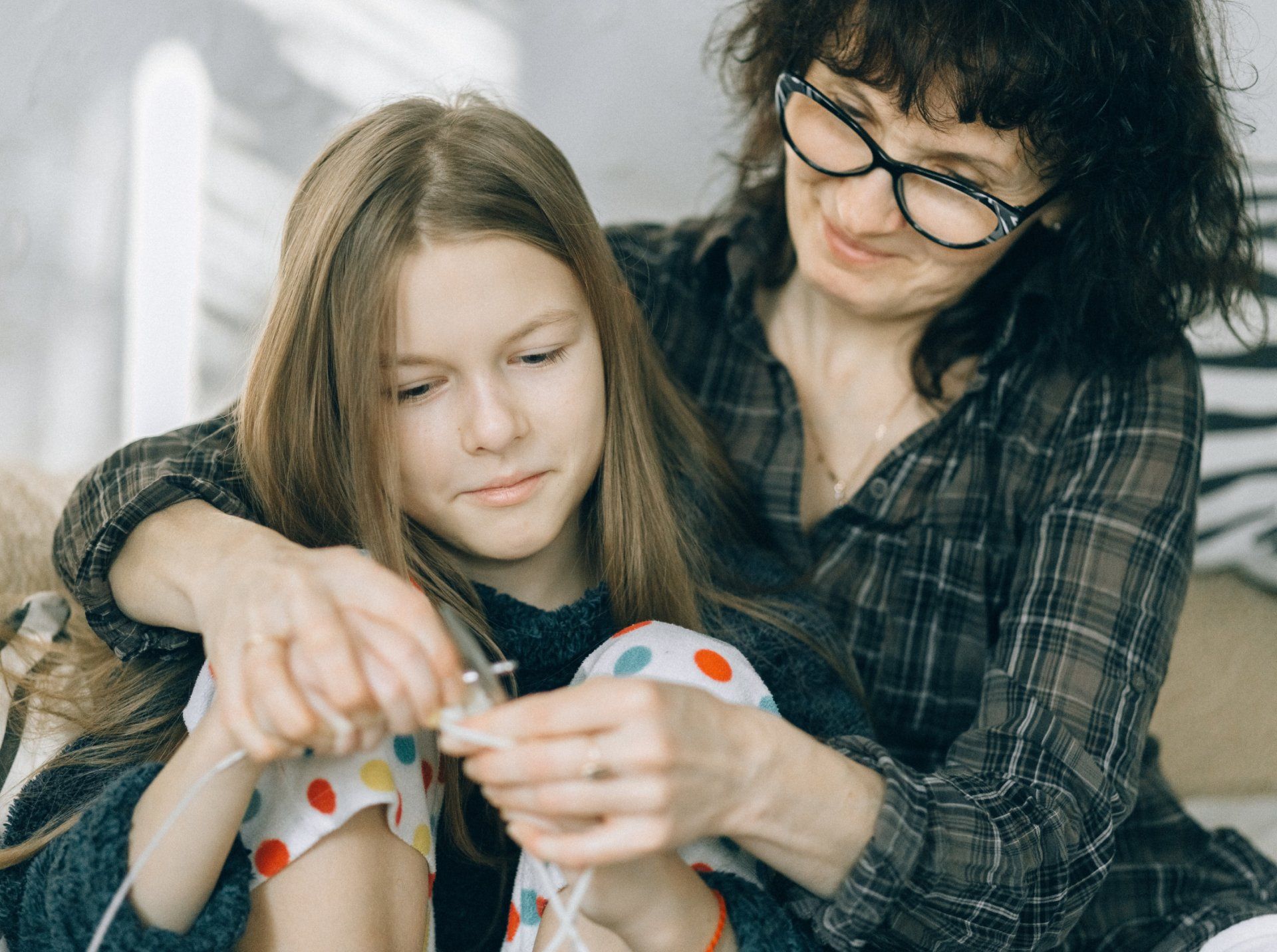 A woman is helping a young girl knit.