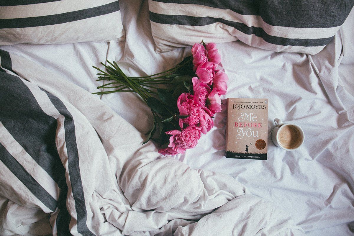 Uma cama com um livro, flores e uma xícara de café.