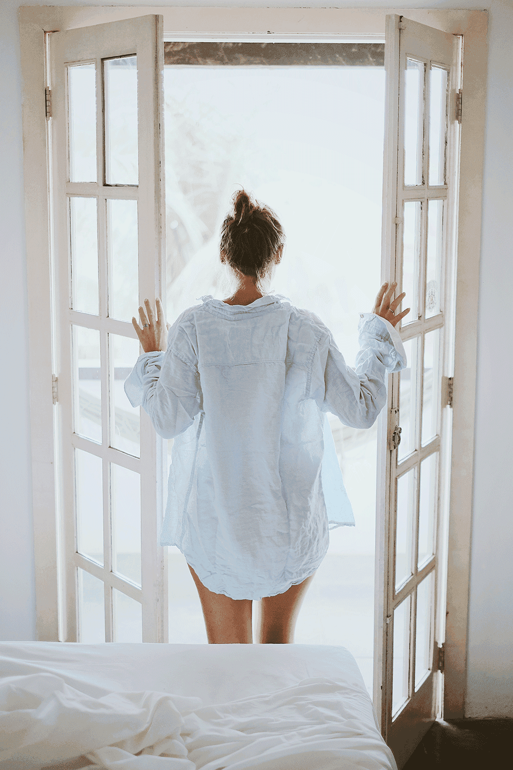 Uma mulher de camisa branca está parada em frente a uma janela.