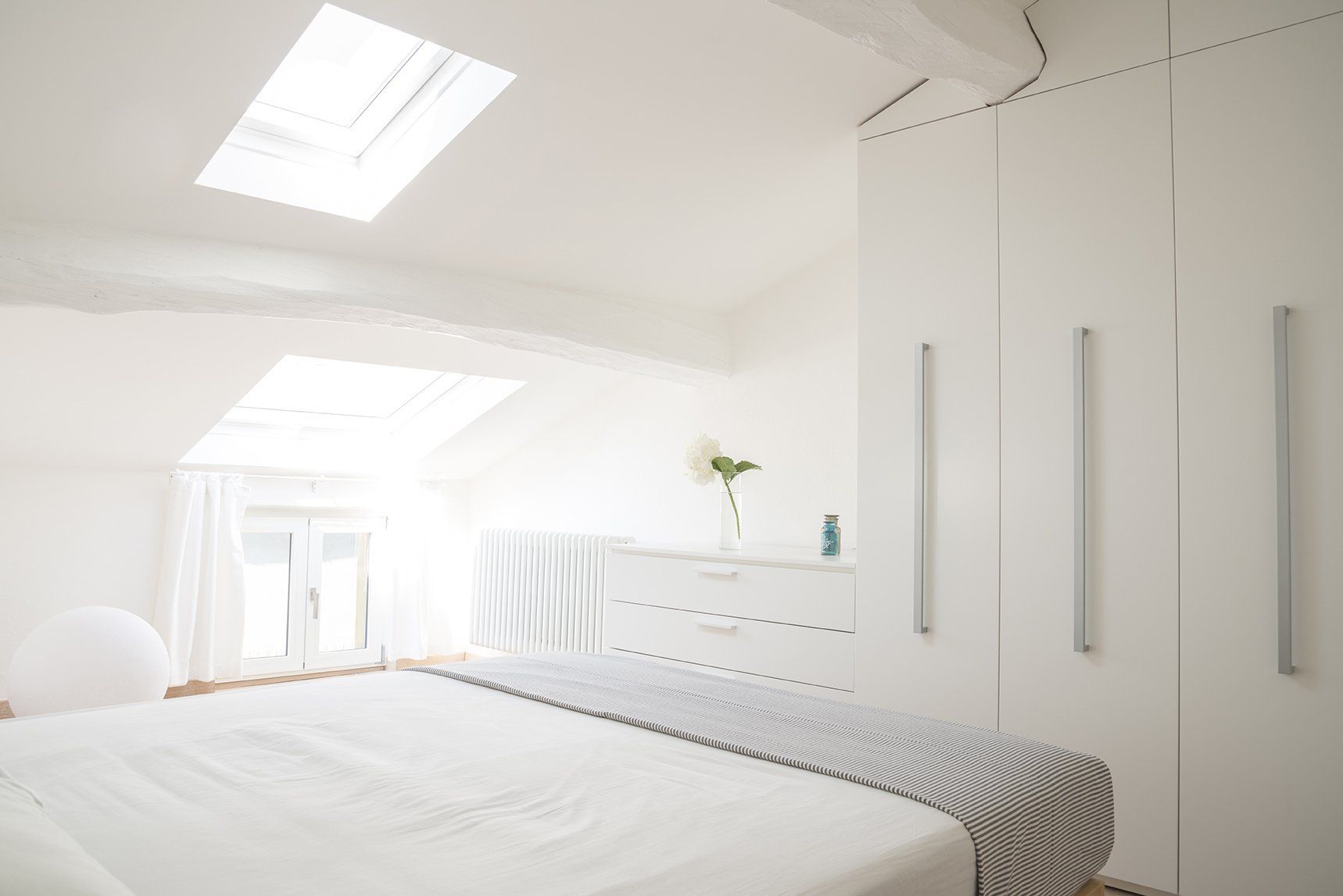 Um quarto com cama, cômoda e clarabóia.