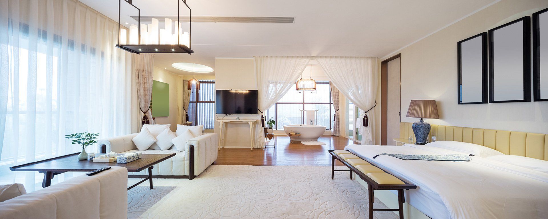 Spacious open-concept bedroom with a living area. White decor and furniture. A large window with curtains.