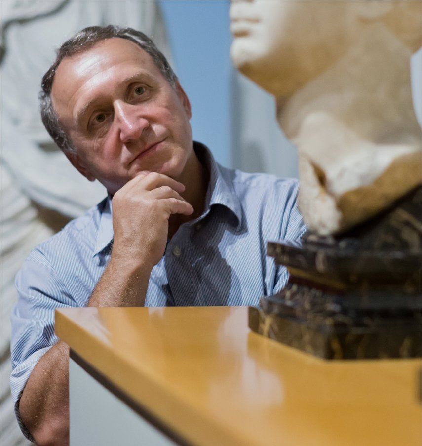 Man in blue shirt, pondering, looking at a white sculpture on display in a museum.
