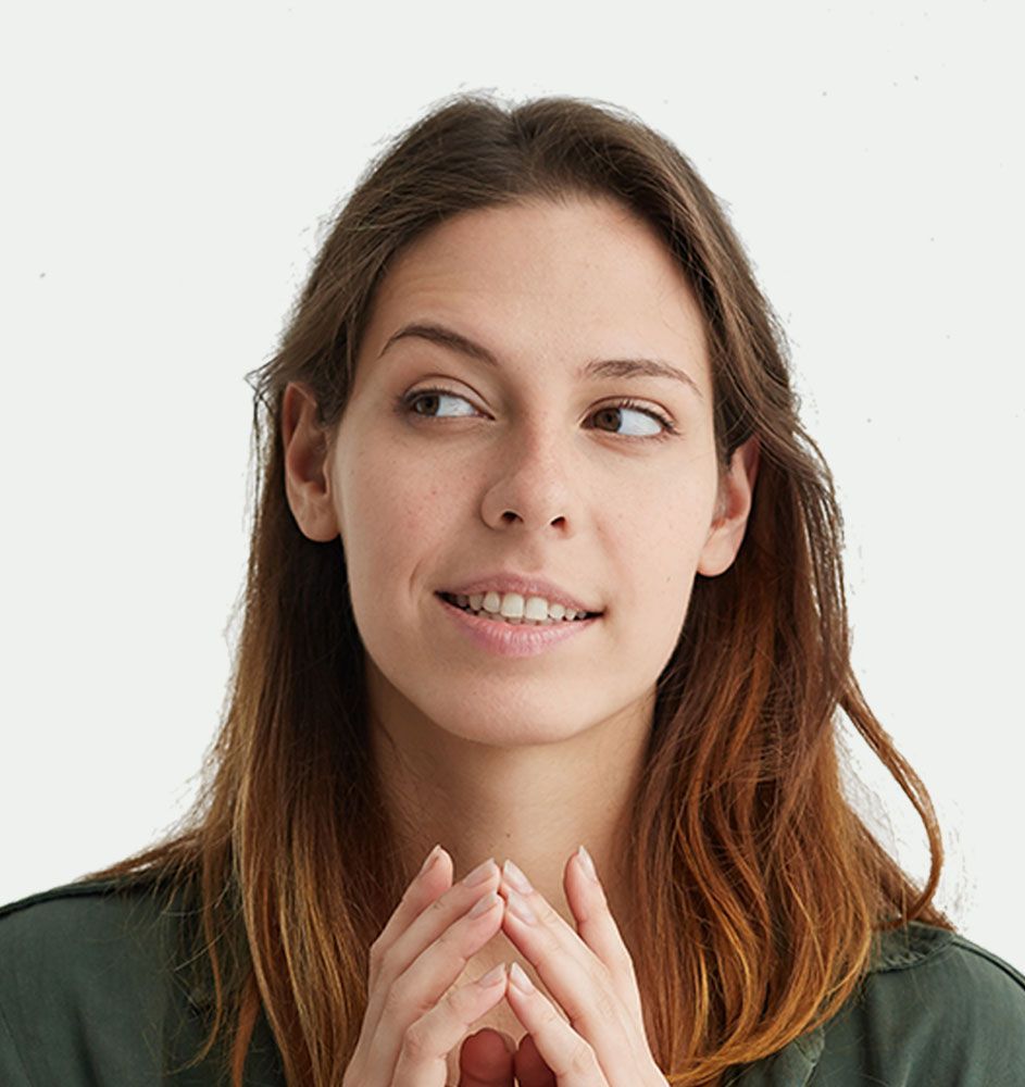 A woman is smiling with her hands folded in front of her face.
