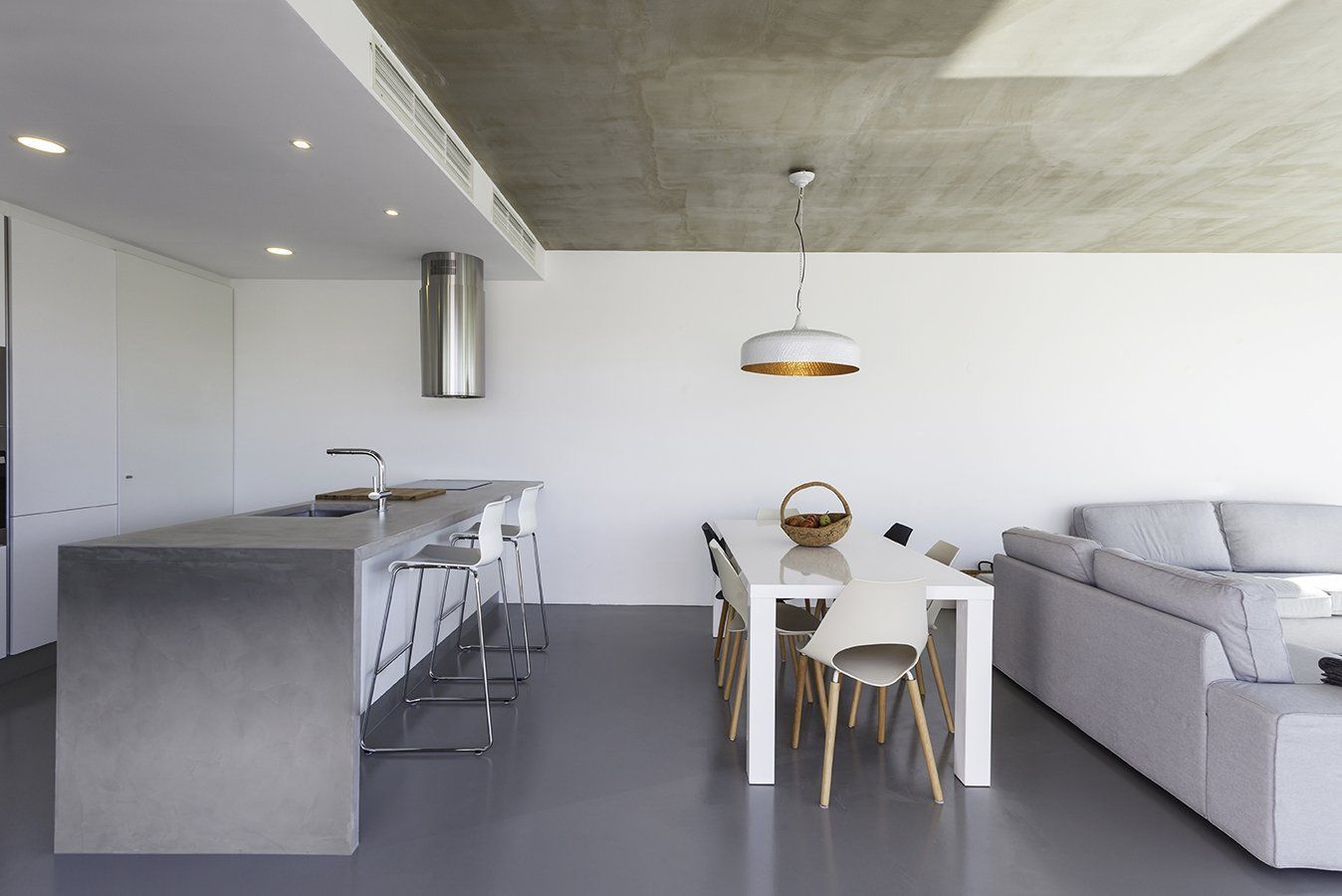 Modern, open-plan kitchen and dining area with white walls, gray floor, metal island, and white table.