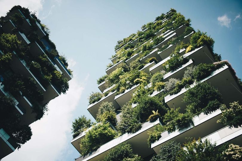 A tall building with lots of balconies covered in plants and trees.