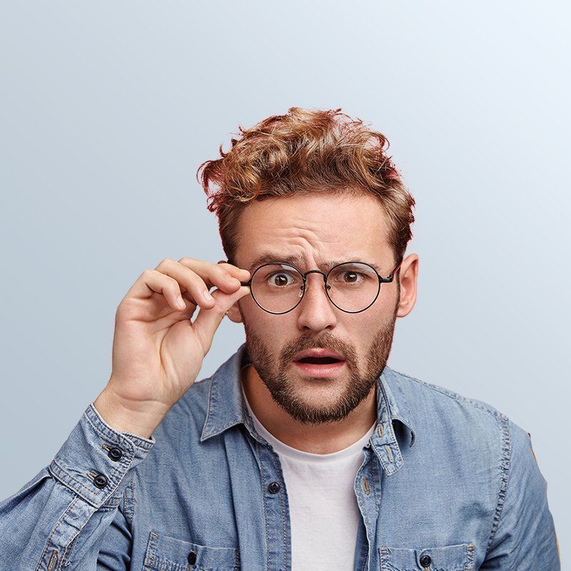 A man wearing glasses and a denim shirt is making a surprised face.