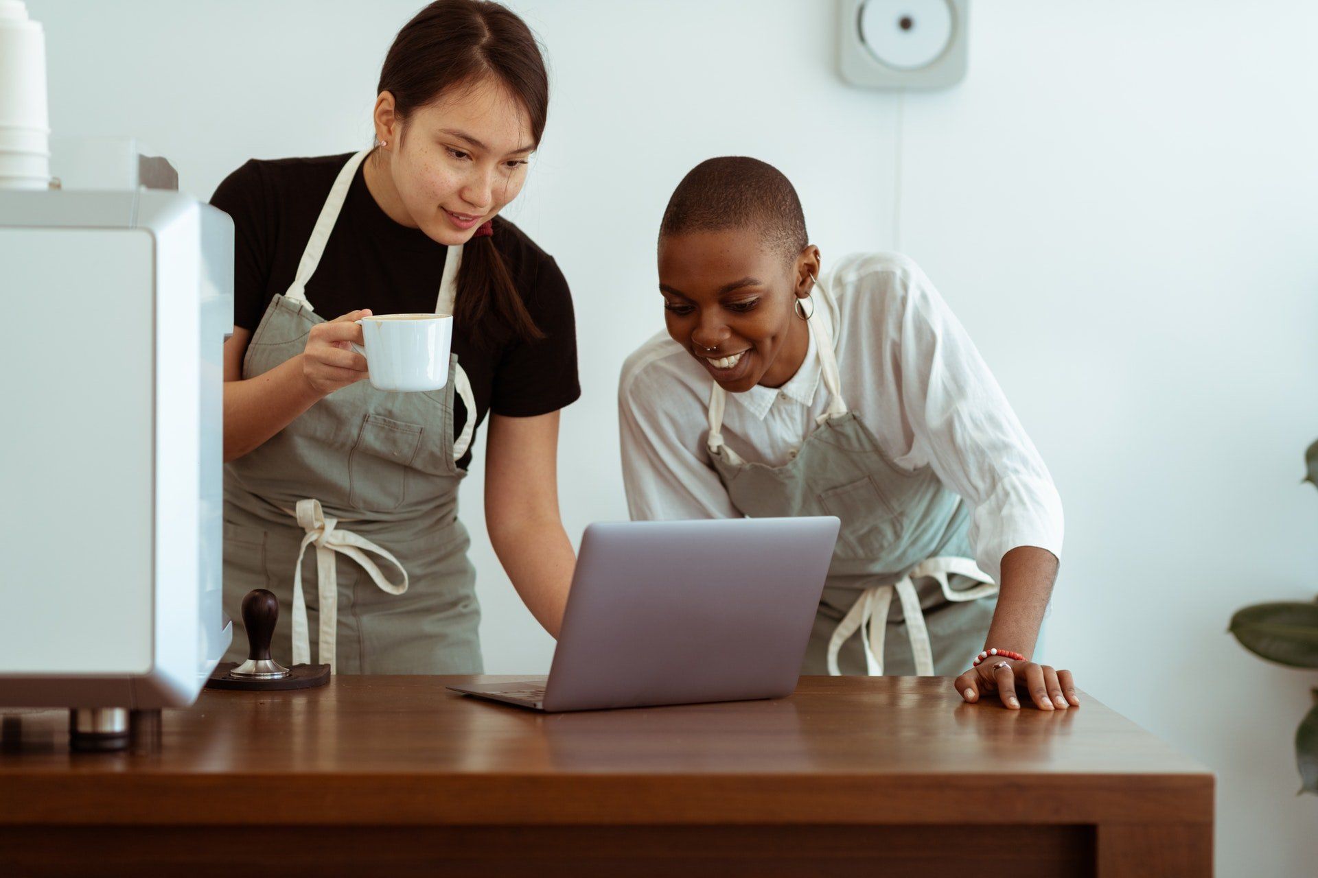 Two women are standing at a table looking at a laptop computer.