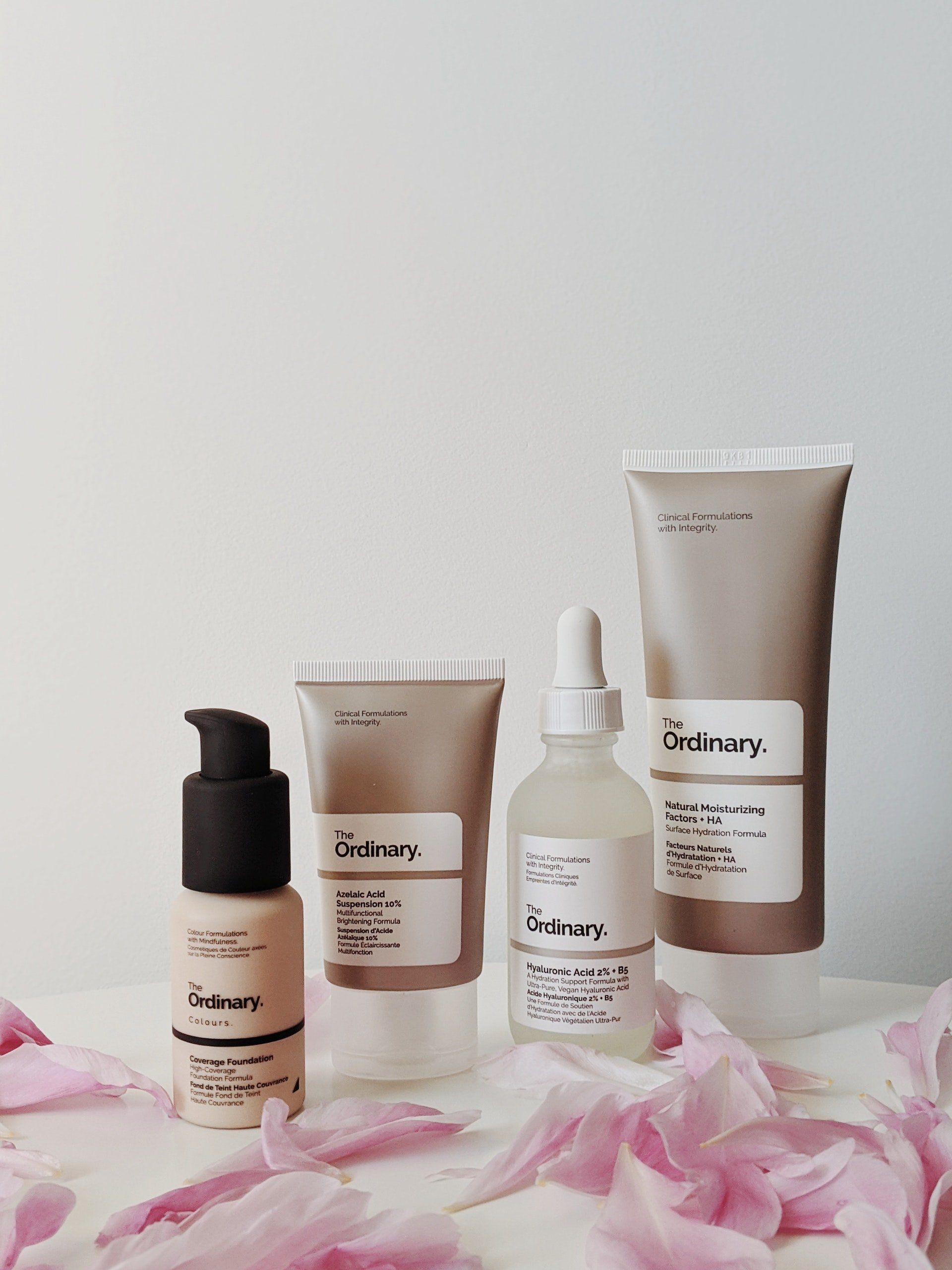 Three bottles of the ordinary cosmetics are sitting on a table surrounded by pink petals.