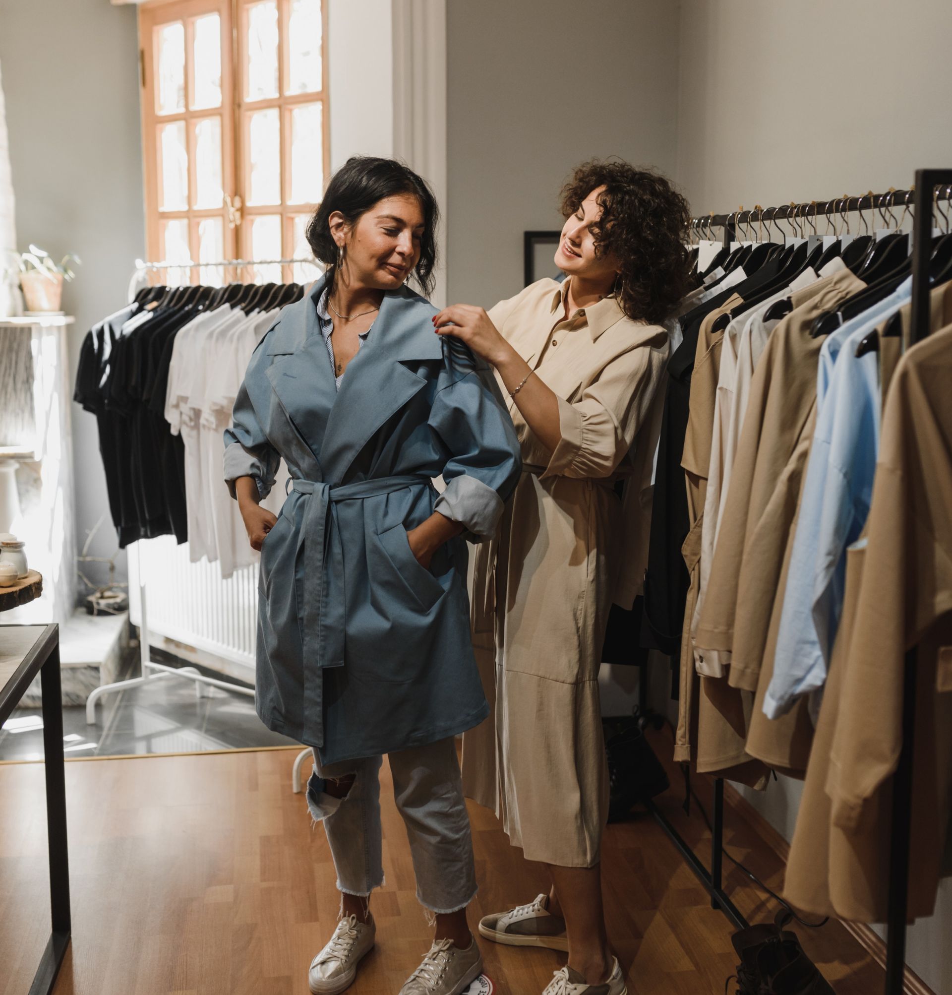 Woman in blue jacket being fitted by a woman in beige dress in a clothing store.