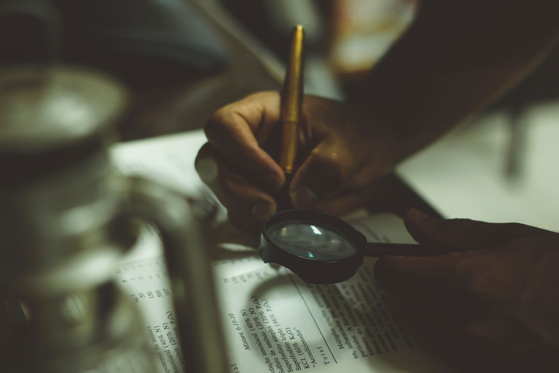 A person is writing on a piece of paper with a magnifying glass
