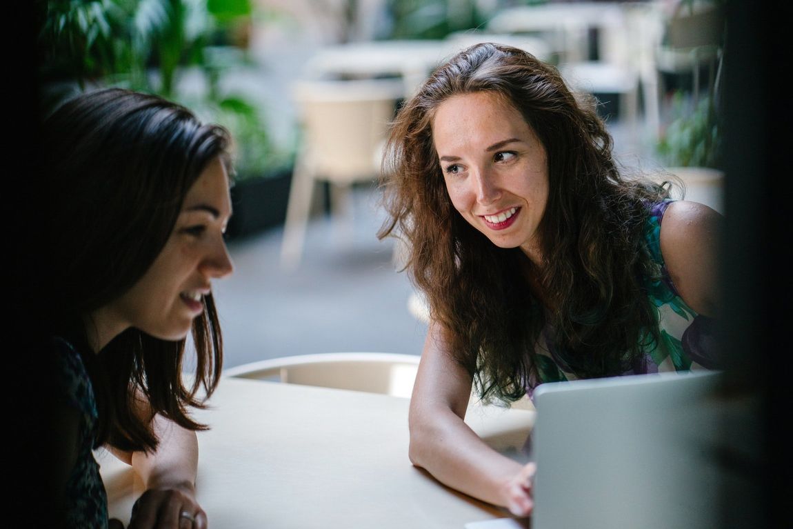 Two women are sitting at a table looking at a laptop computer.