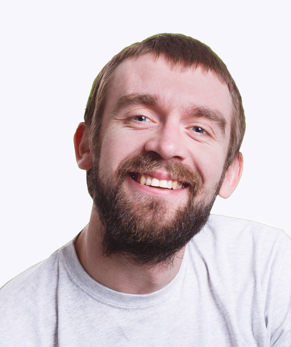 A man with a beard is smiling and wearing a grey shirt
