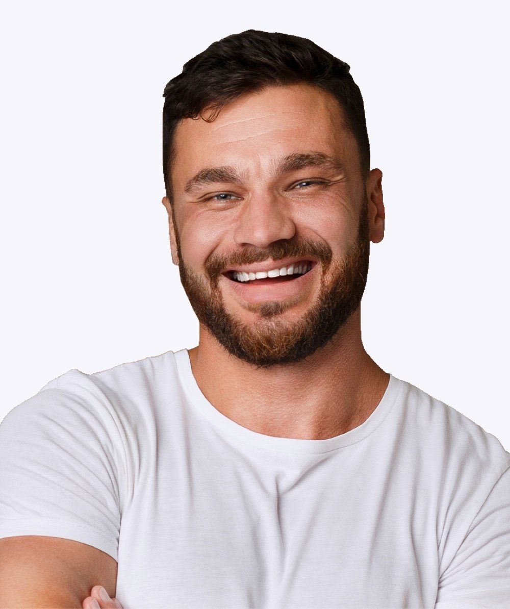 A man with a beard is wearing a white t-shirt and smiling.