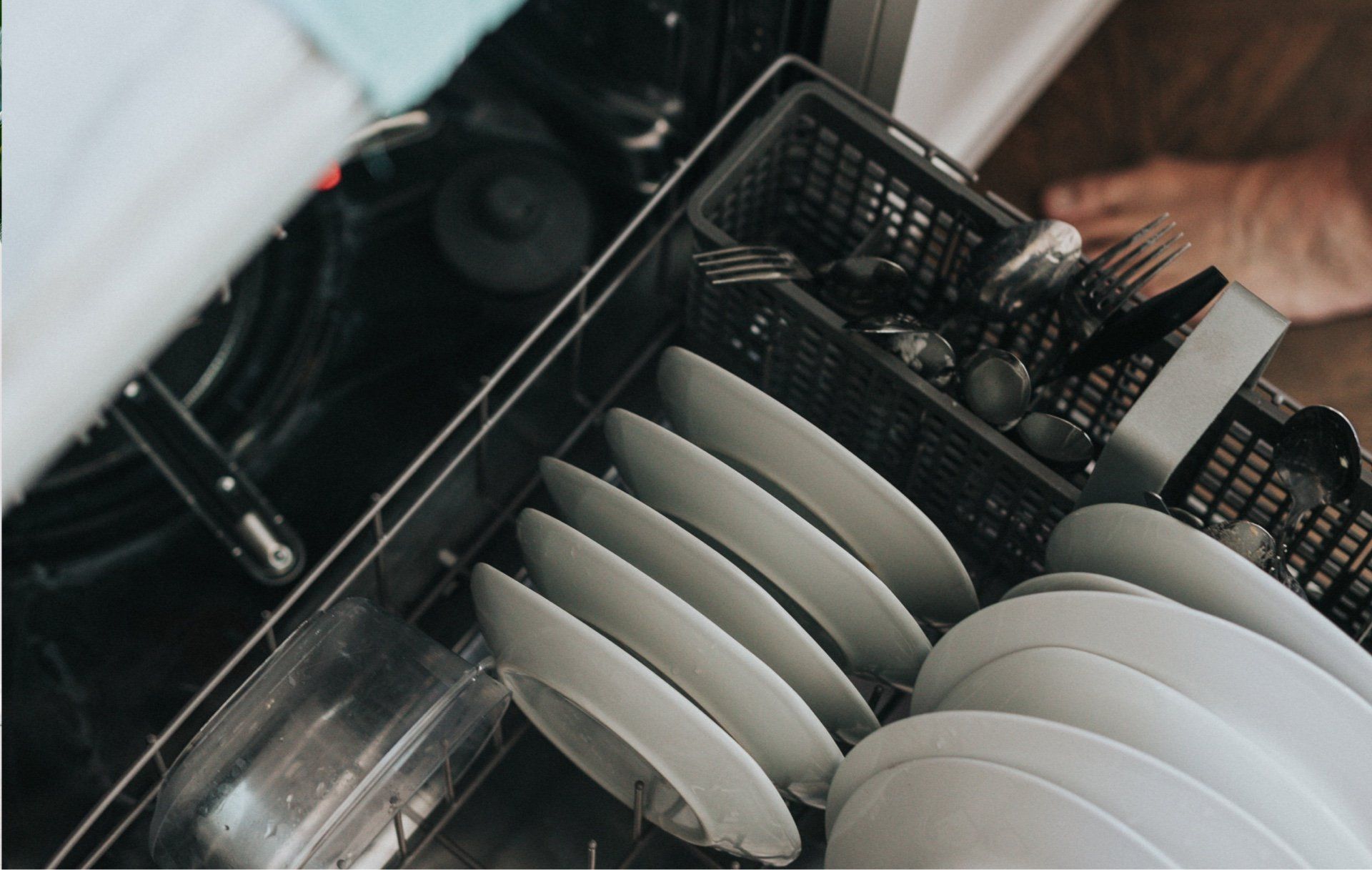 A person is loading plates and silverware into a dishwasher.