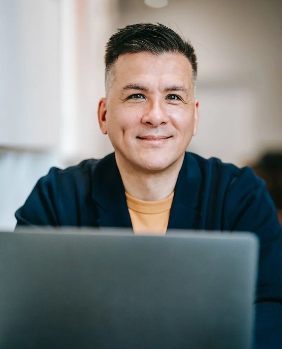 A man is sitting in front of a laptop computer and smiling.