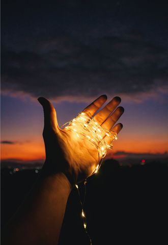 Hand holding glowing string lights against a sunset sky.