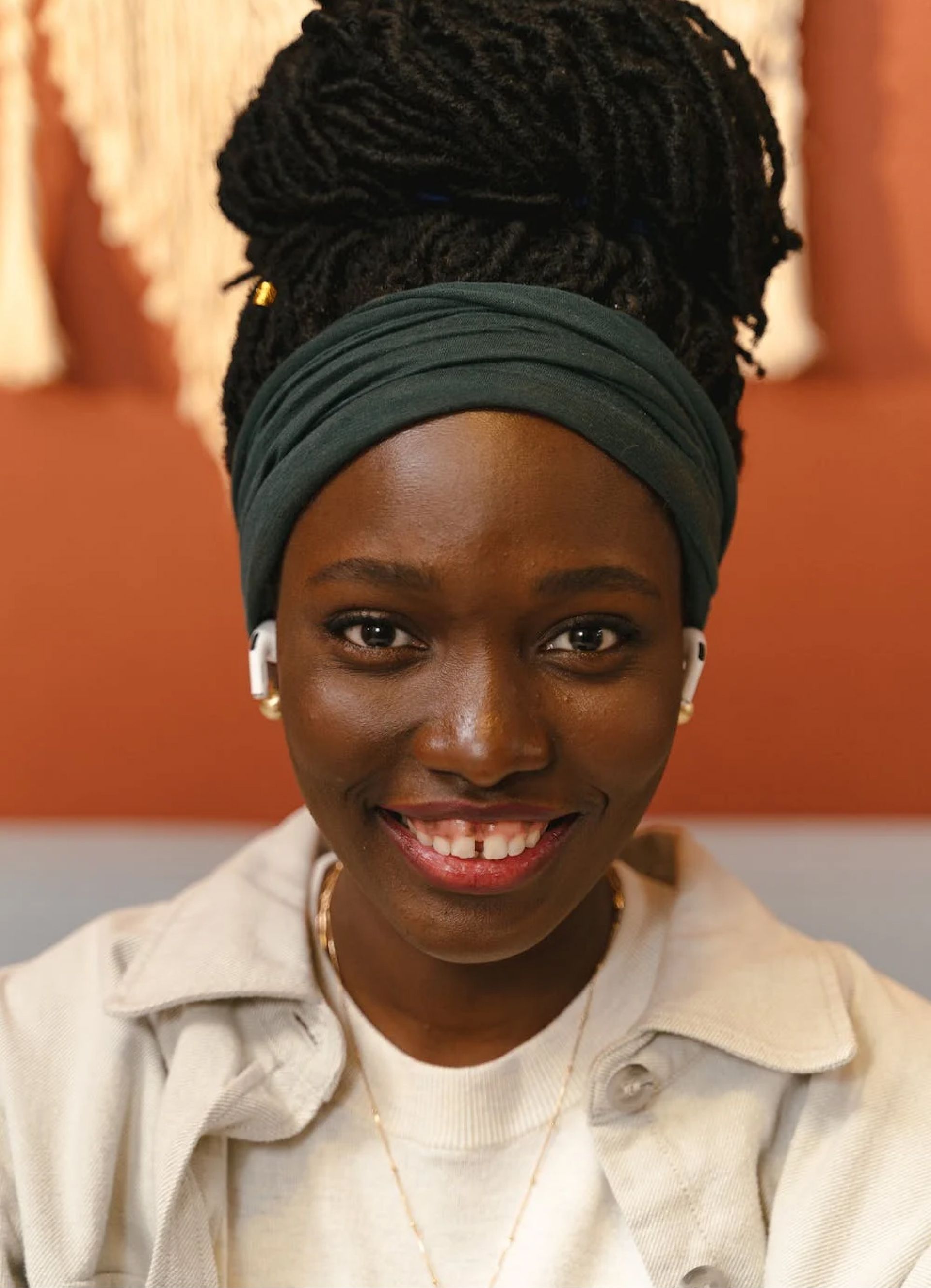Woman with locs up in a bun, wearing a green headband and a gray jacket, smiling at the camera.