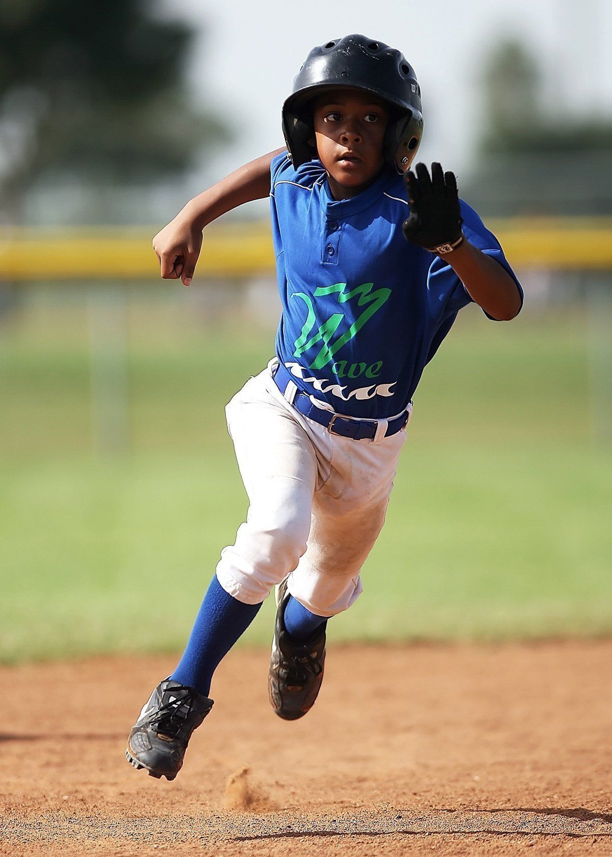 A young boy in a blue shirt and white pants is running on a baseball field.