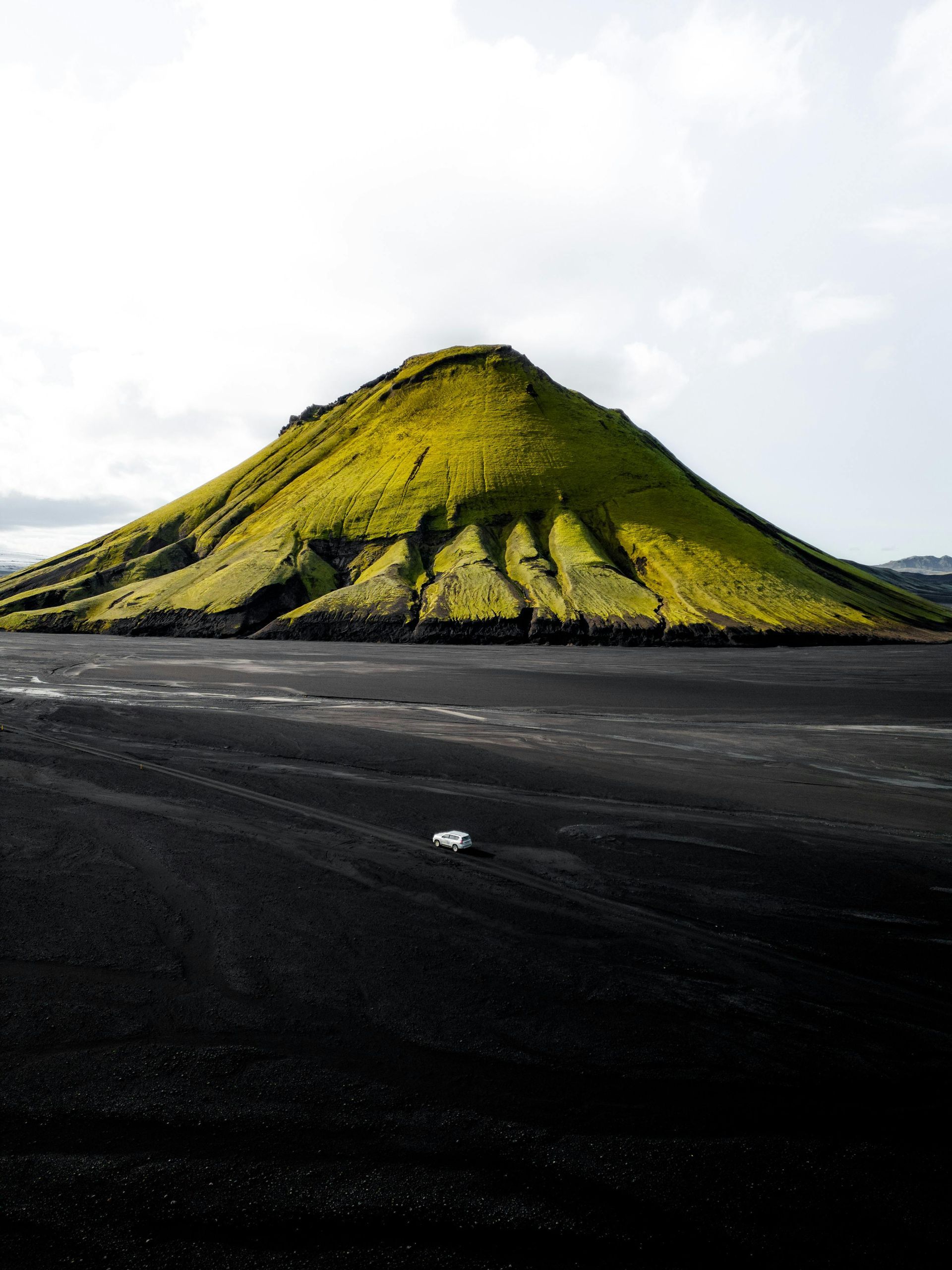 Green hill rises from a black sand plain; overcast sky.