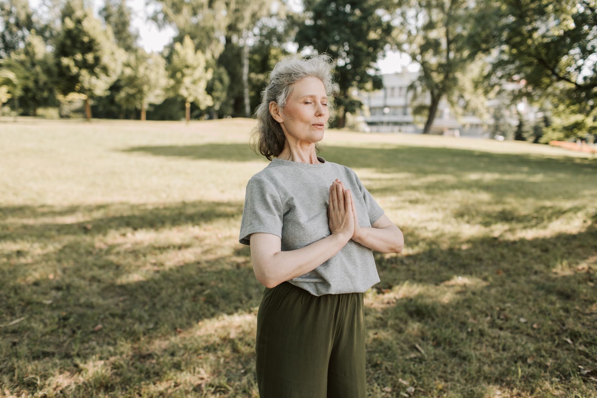 An elderly woman is practicing yoga in a park.