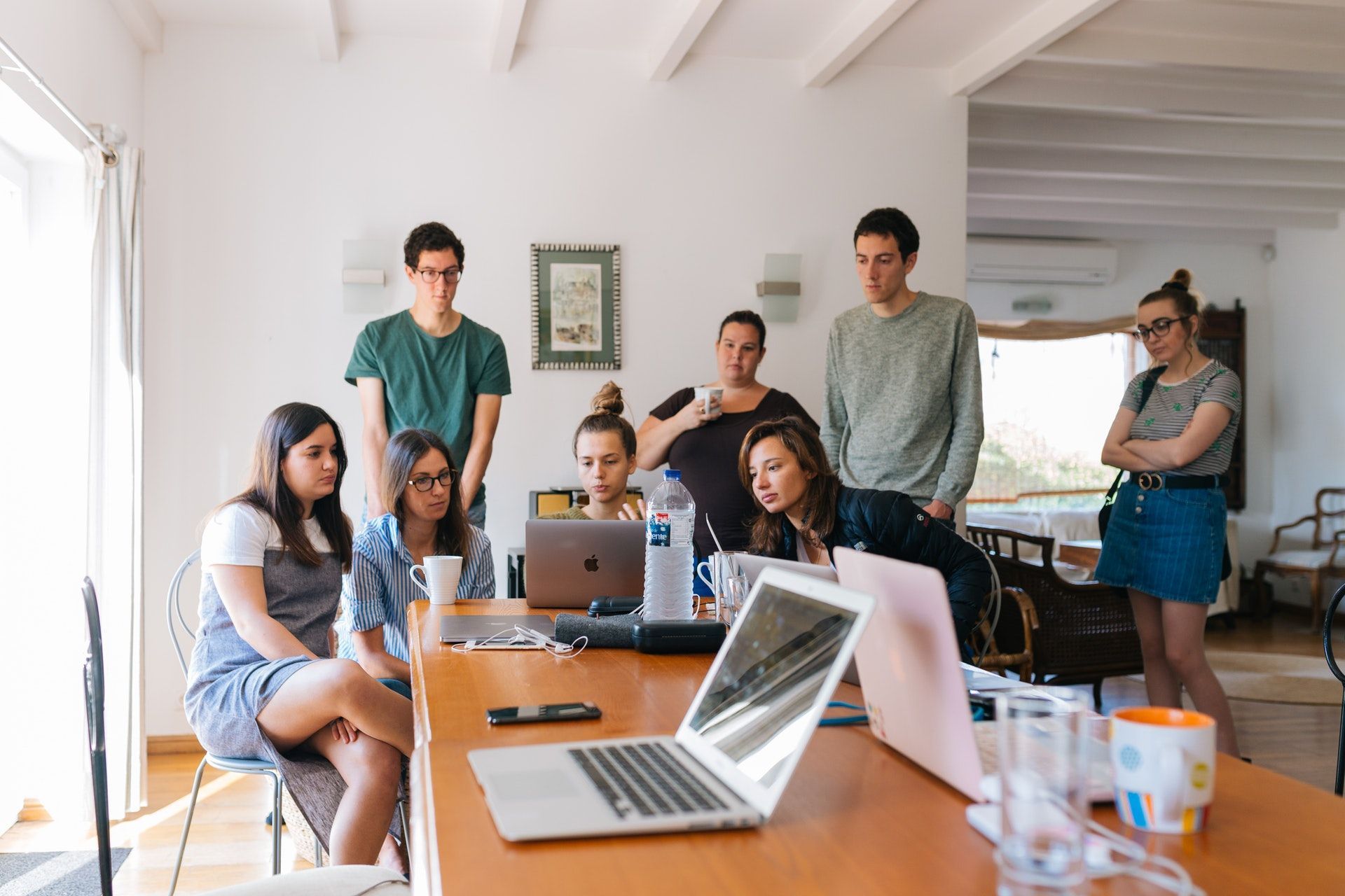 A group of people are sitting around a table with laptops.