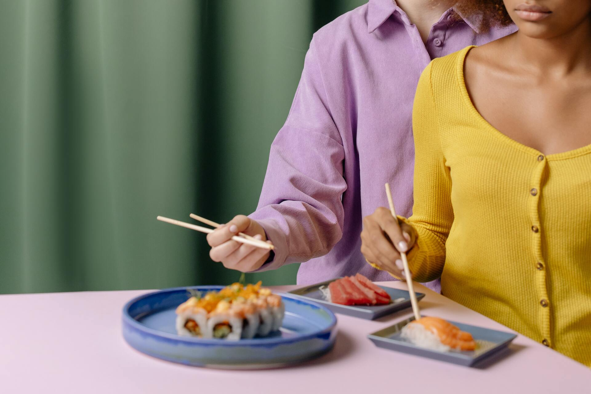 A man and a woman are sitting at a table eating sushi with chopsticks.