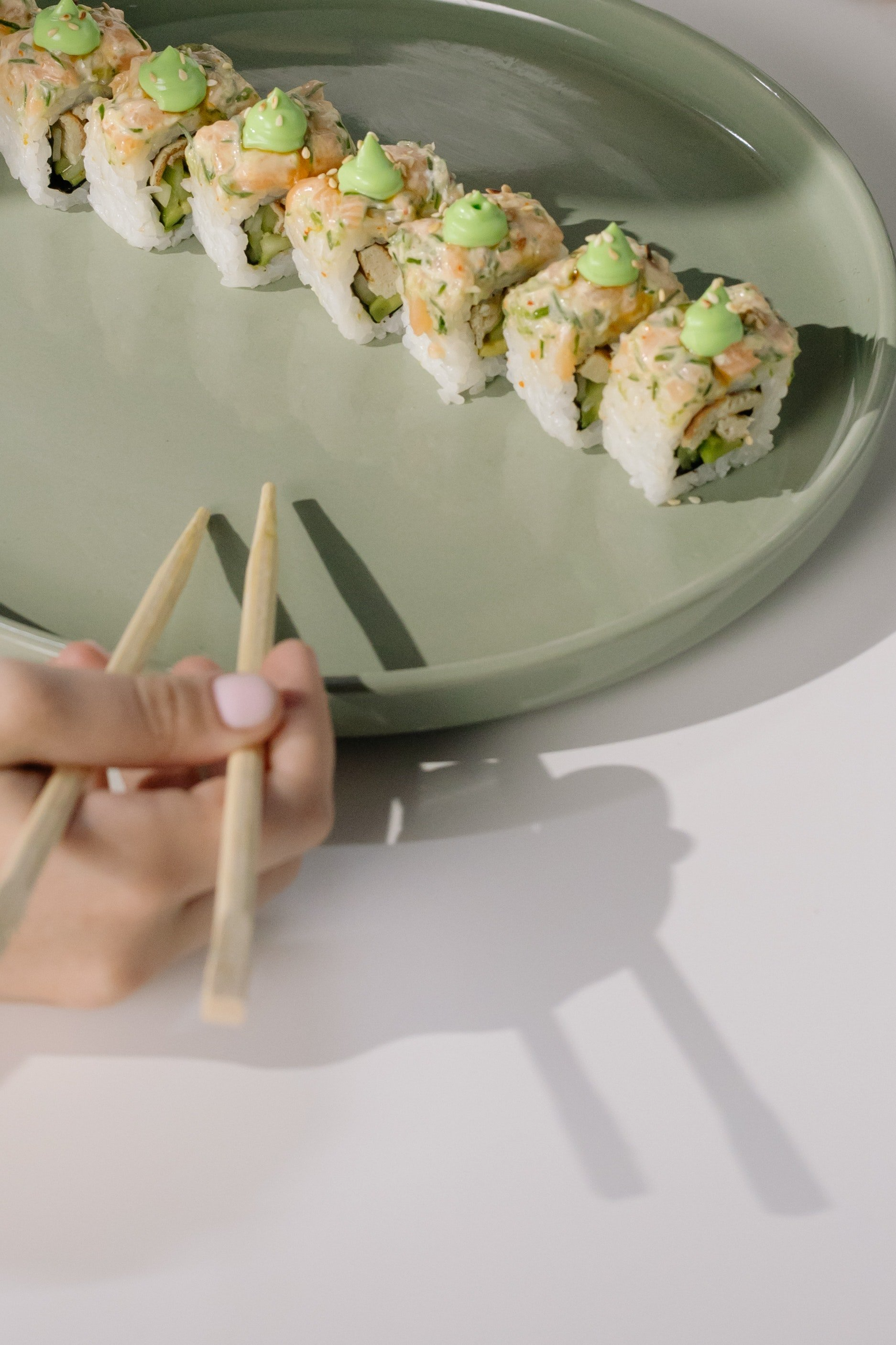 A person is holding chopsticks in front of a plate of sushi.