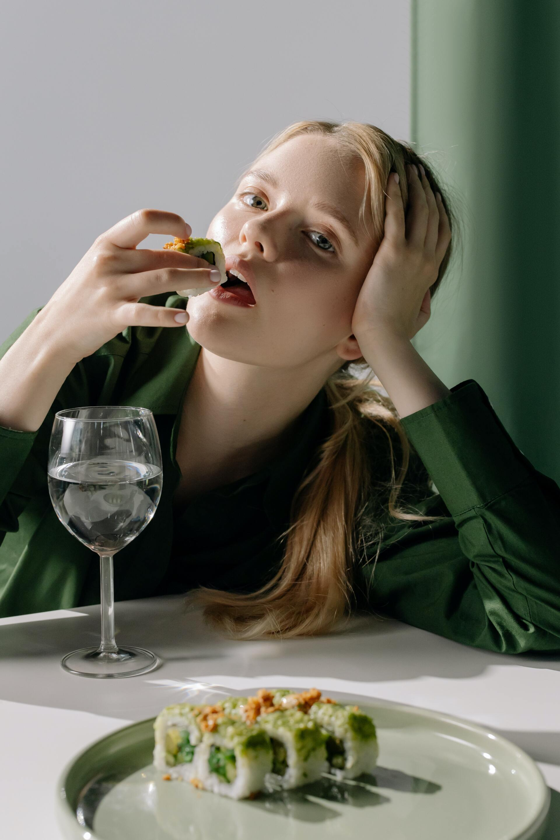 A woman is sitting at a table eating sushi and drinking wine.