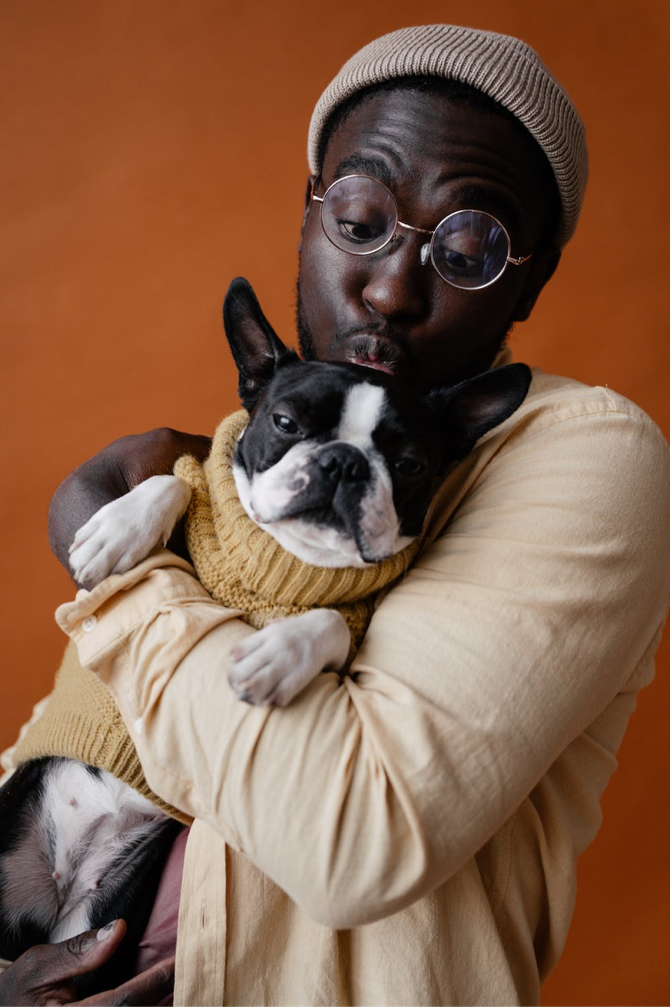 A man is holding a dog in his arms and the dog is wearing a sweater.