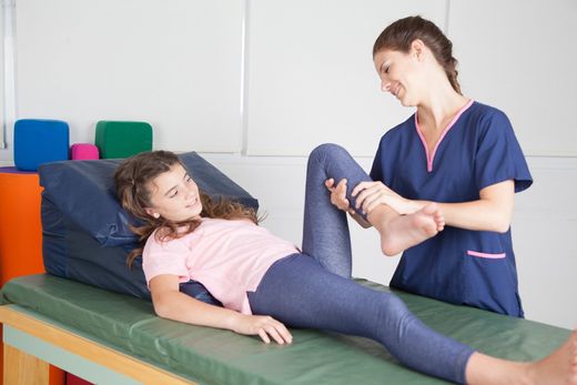 A young girl receives physical therapy on her leg from a therapist in a clinical setting.