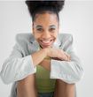 A woman in a white jacket is smiling with her hands on her face