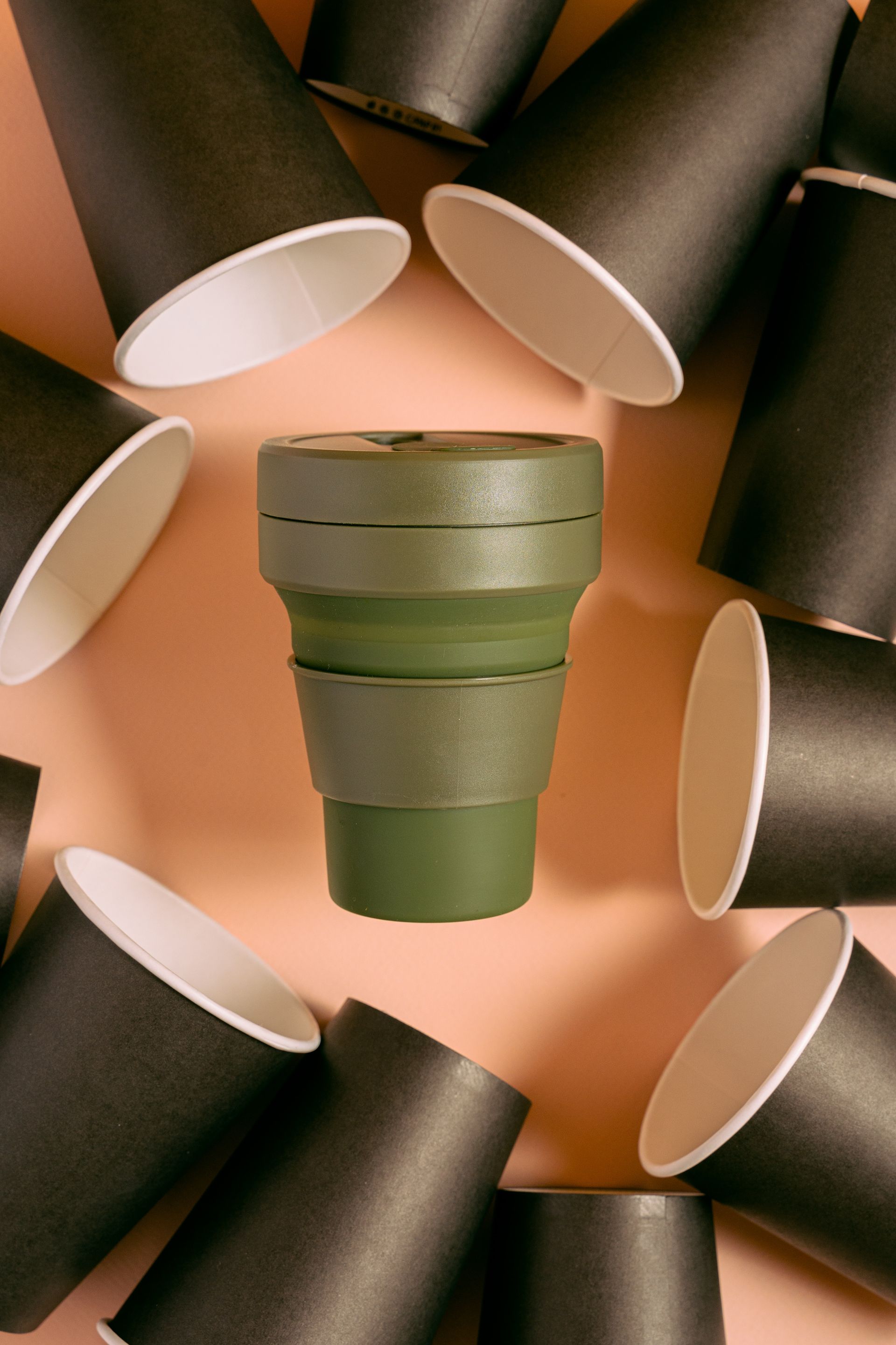 A green cup is surrounded by black cups on a table.