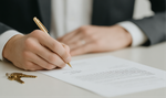 Person signing a document with a gold pen, keys on the table.
