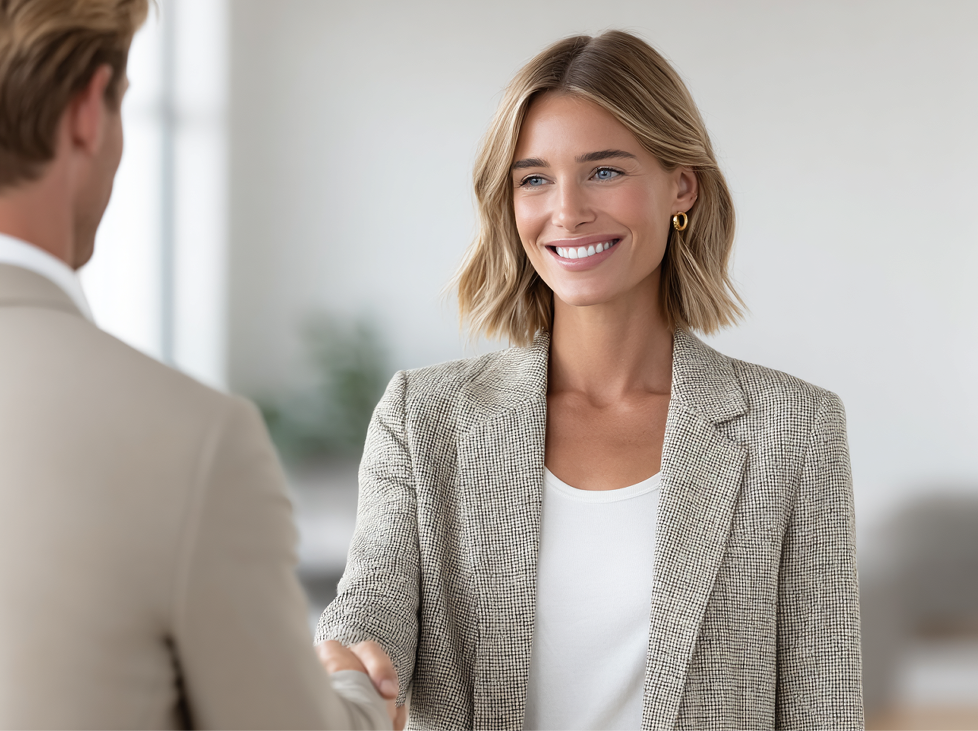 Woman in blazer shaking hands with a person in a suit, smiling, indoors.
